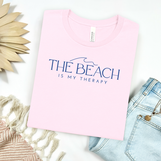 Bella Canvas 3001 "The Beach Is My Therapy" t shirt with a simple wave graphic with text and one color graphic. Picture on a flay lay mockup with pair of blue jeans and blanket and a wicker sun shaped accessory.
