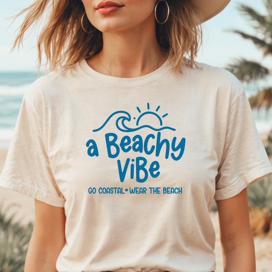 Person wearing a t-shirt with 'a Beachy ViBe' text on a beach.