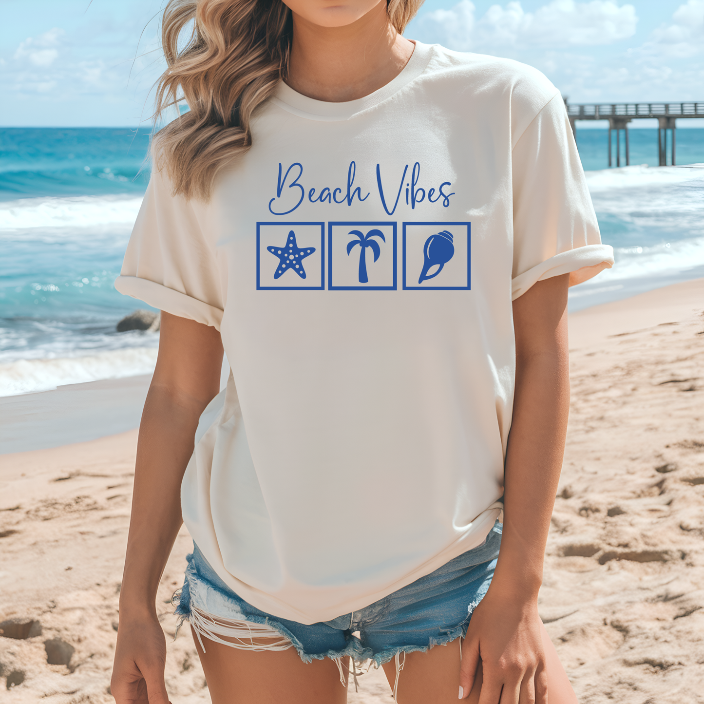 Bella and Canvas 3001 "Beach Vibes" t shirt with a starfish, palm tree, and a seashell graphics in monochrome color. Picture of a girl standing on the beach wearing a t shirt.