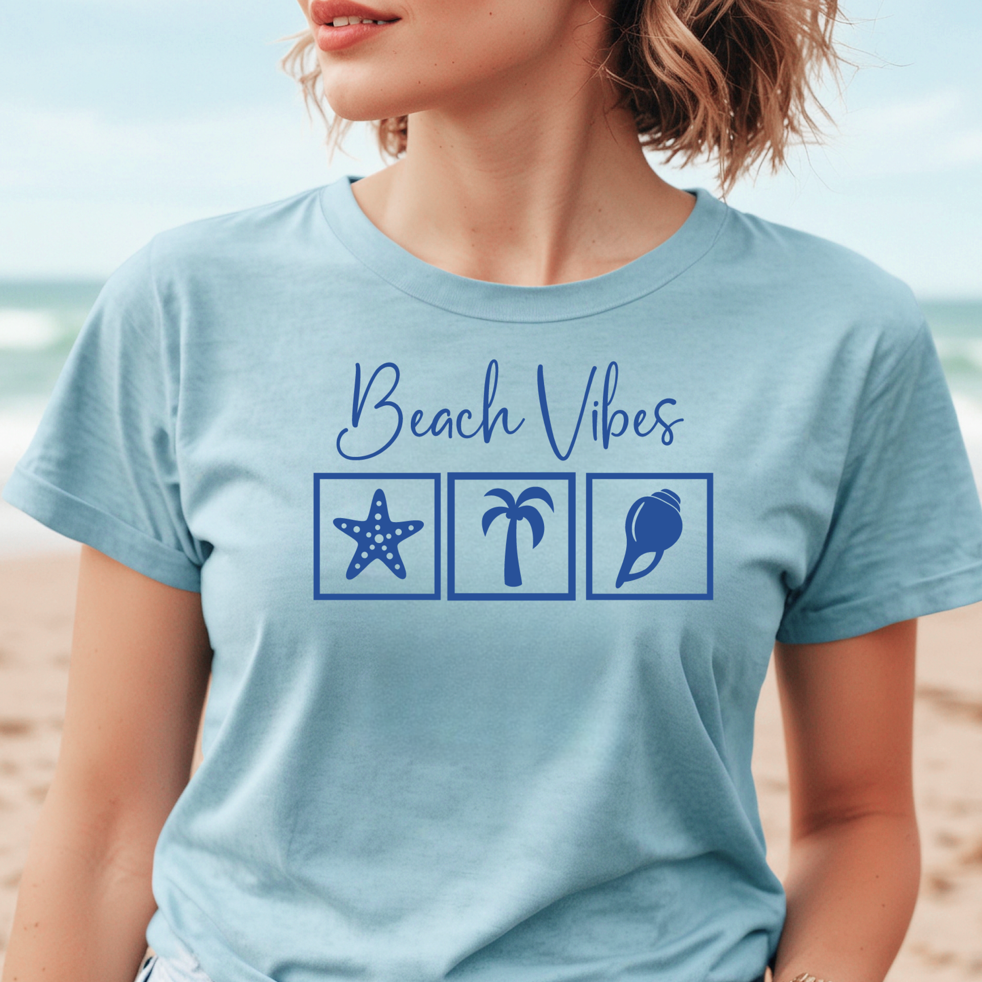 Bella and Canvas 3001 "Beach Vibes" t shirt with a starfish, palm tree, and a seashell graphics in monochrome color. Picture of a girl standing on the beach wearing a t shirt.