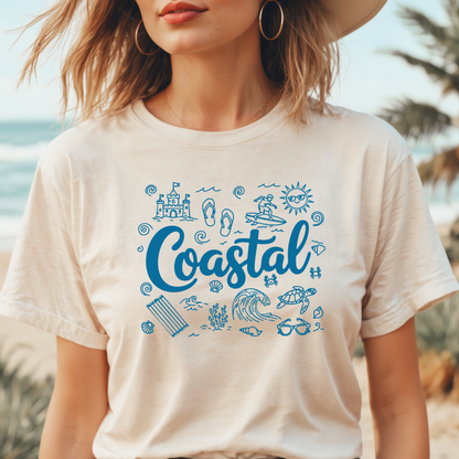 Person wearing a natural colored t-shirt with blue 'Coastal' design and beach icons, standing by the ocean.