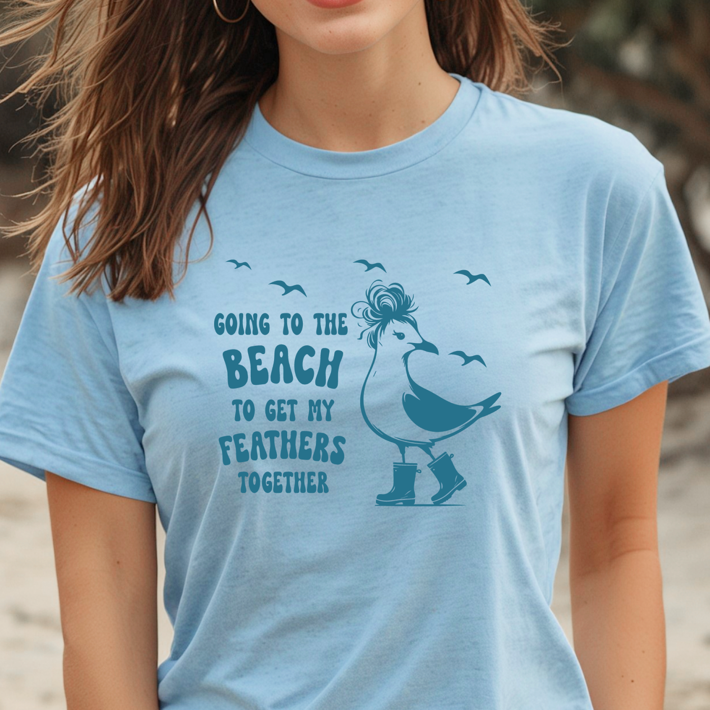 Person wearing a light blue t-shirt with a seagull graphic and text on a beach.
