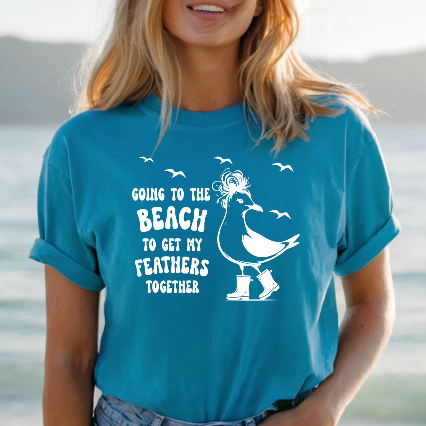 Person wearing a aqua blue t-shirt with a beach-themed design and text.