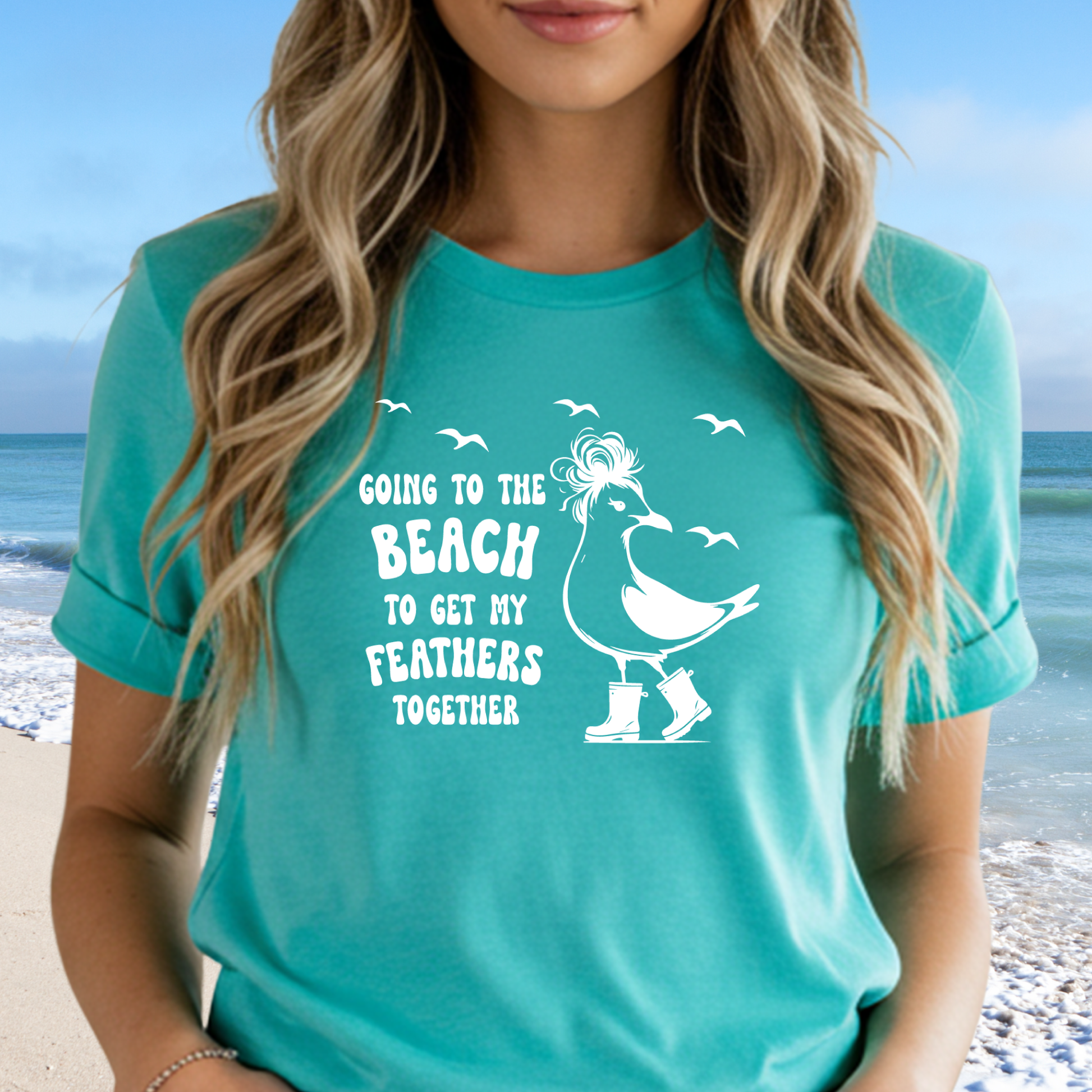 Person wearing a teal t-shirt with a beach-themed graphic and text on a beach background