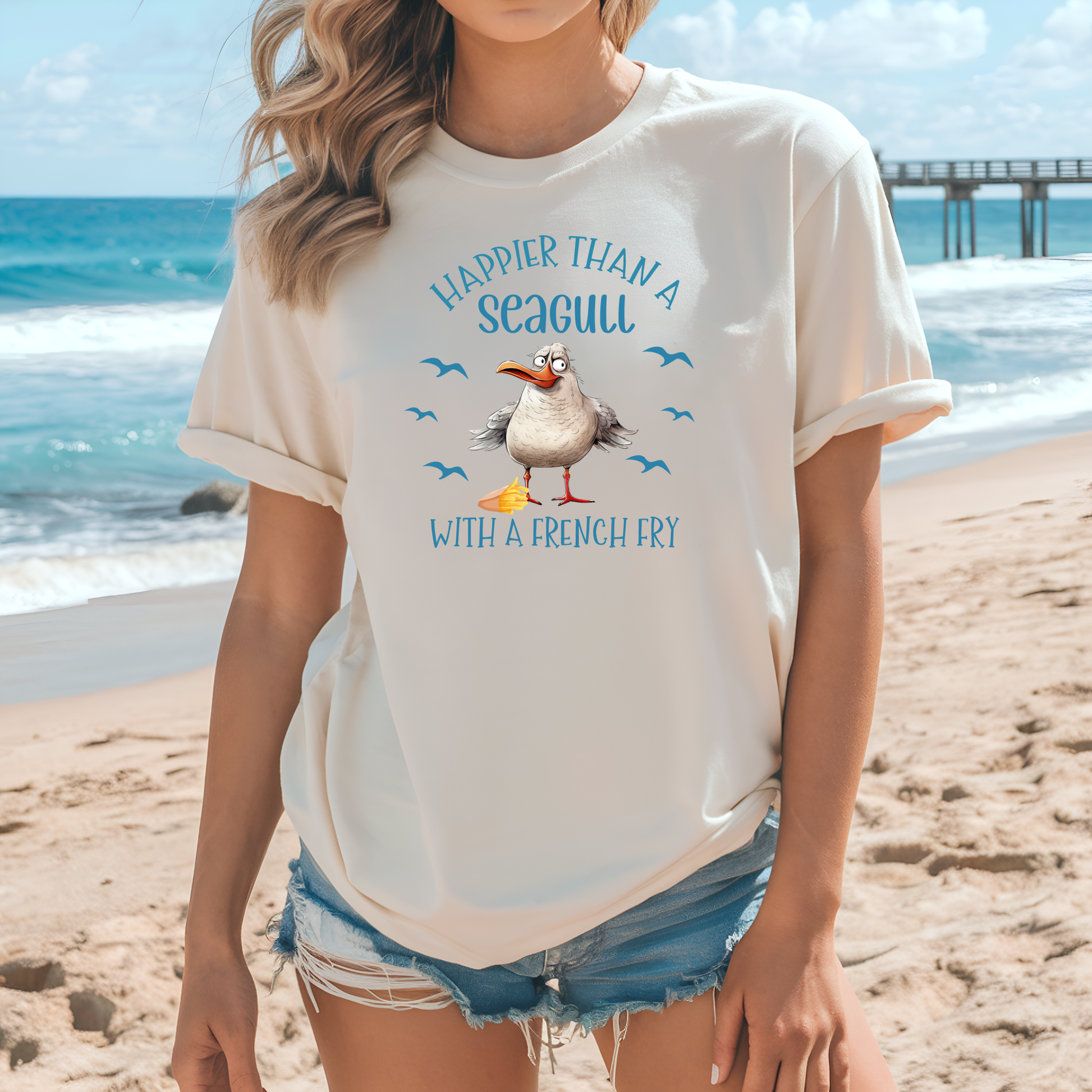 Bella and Canvas 3001 "Happier Than A Seagull With A French Fry" t shirt with an illustration of a seagull with a box of French fries and seagulls flying in the air. Picture of a girl standing on the beach wearing a t shirt.