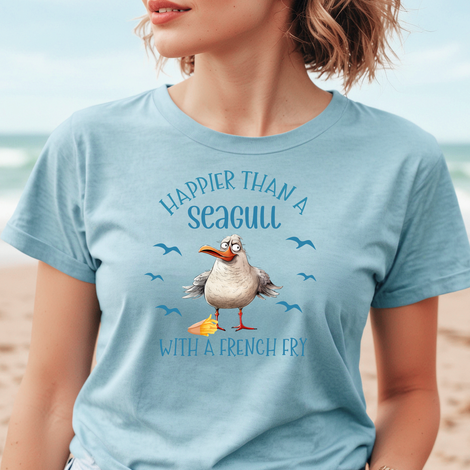 Bella and Canvas 3001 "Happier Than A Seagull With A French Fry" t shirt with an illustration of a seagull with a box of French fries and seagulls flying in the air. Picture of a girl standing on the beach wearing a t shirt.