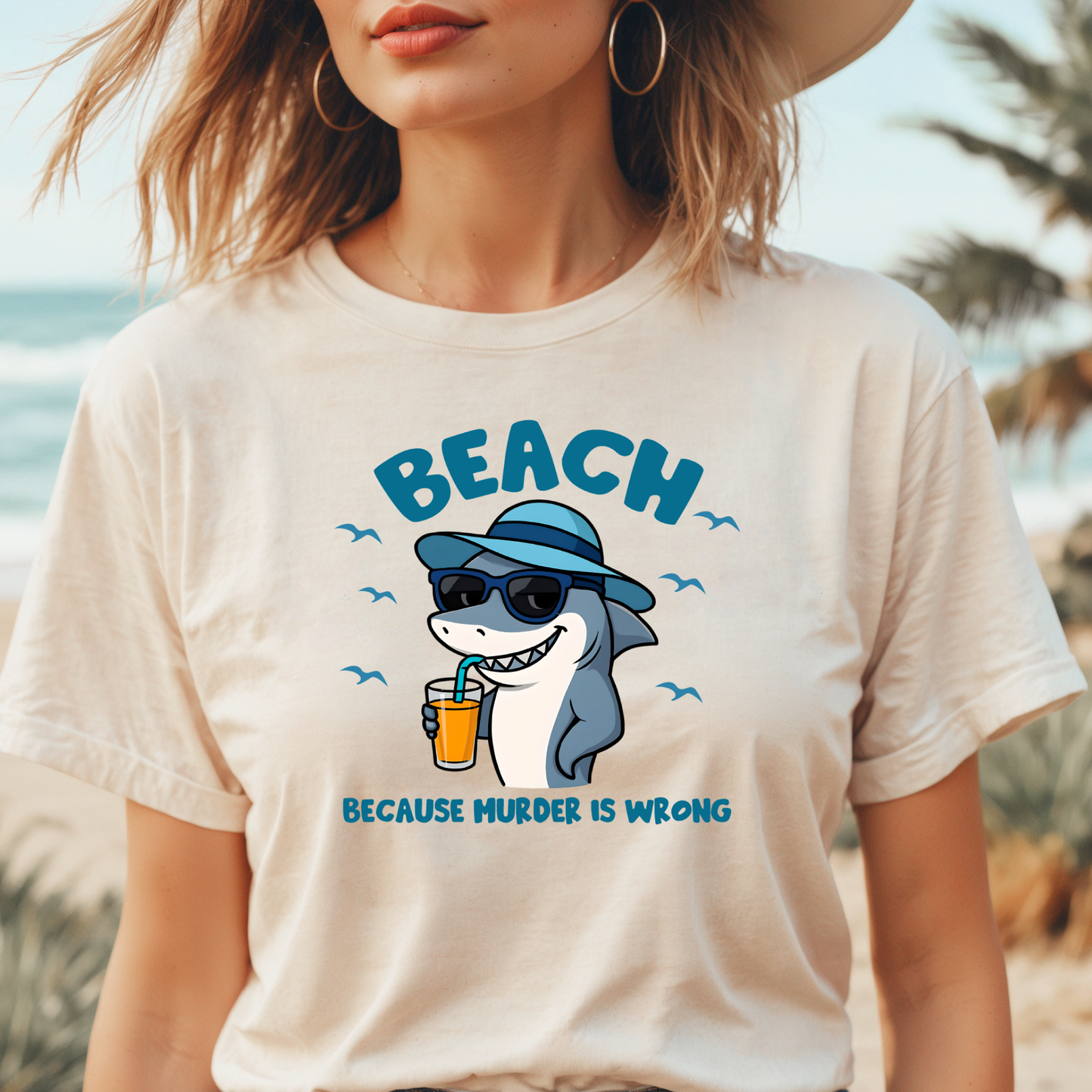 Person wearing a t-shirt with a shark graphic and text on a beach.