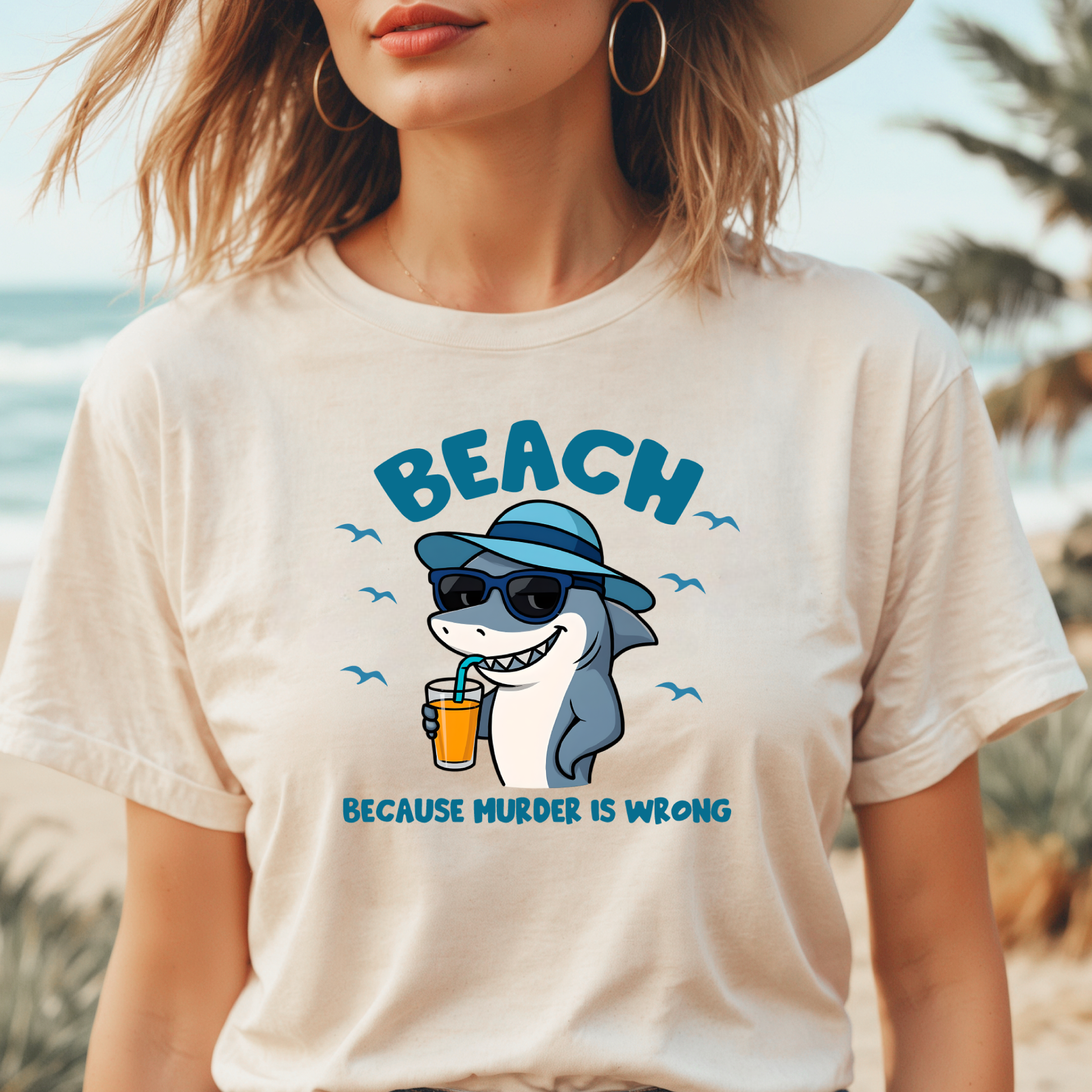 Person wearing a t-shirt with a shark graphic and text on a beach.