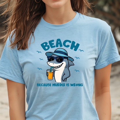 Person wearing a light blue t-shirt with a shark graphic and text on a beach.