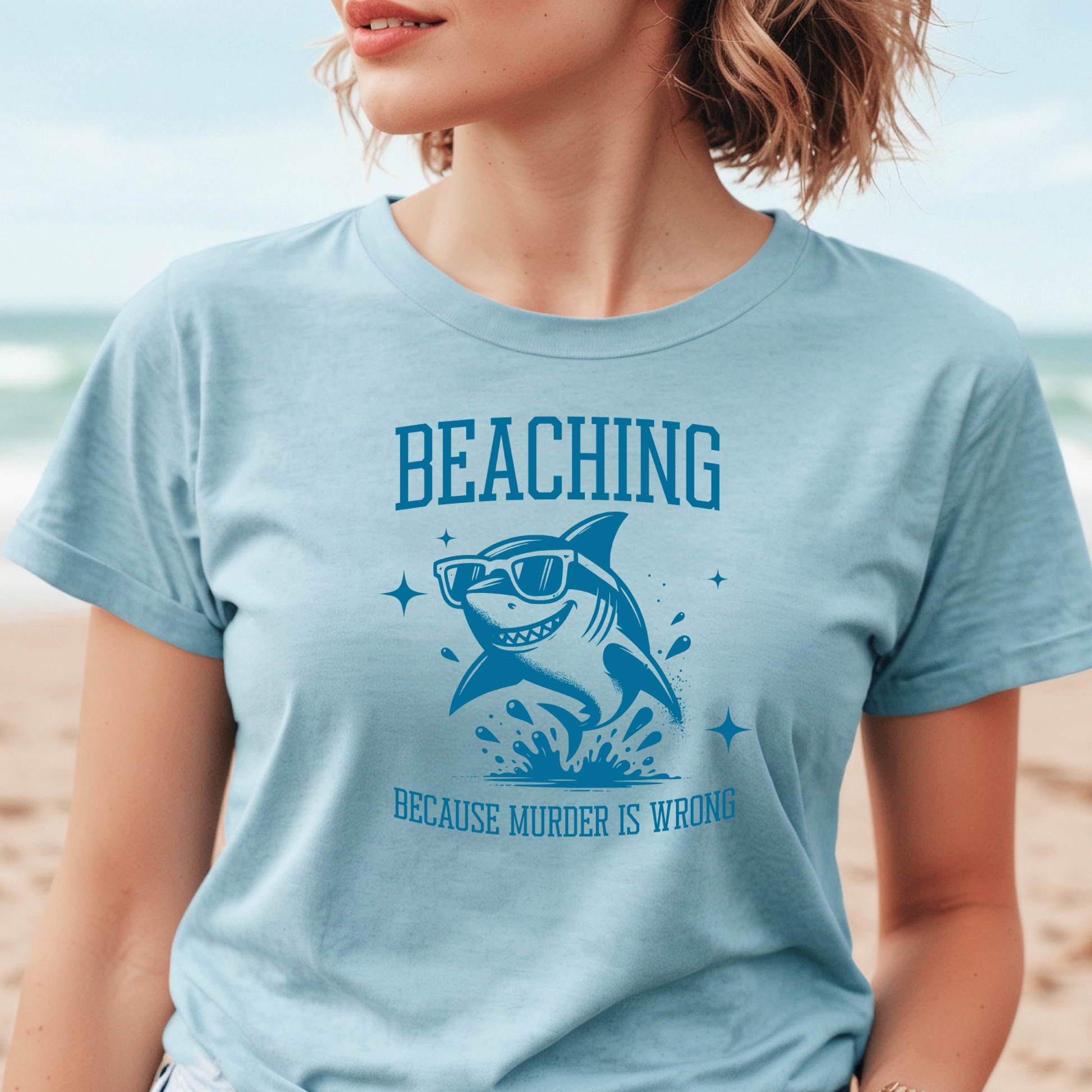 Bella Canvas 3001 Beaching Because Murder Is Wrong  T Shirt with Funny Shark with Sunglasses splashing in water in one color graphic. Picture of a girl standing on the beach wearing a t shirt.