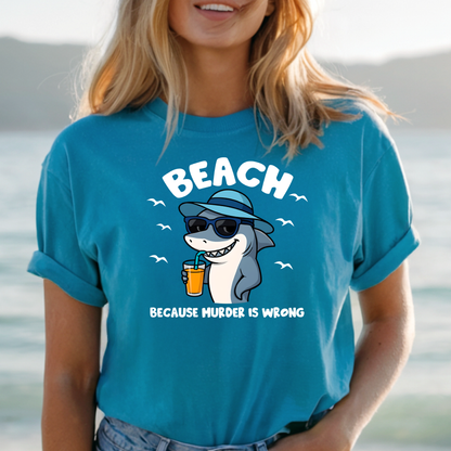 Person wearing a blue t-shirt with a shark graphic and text by a body of water.