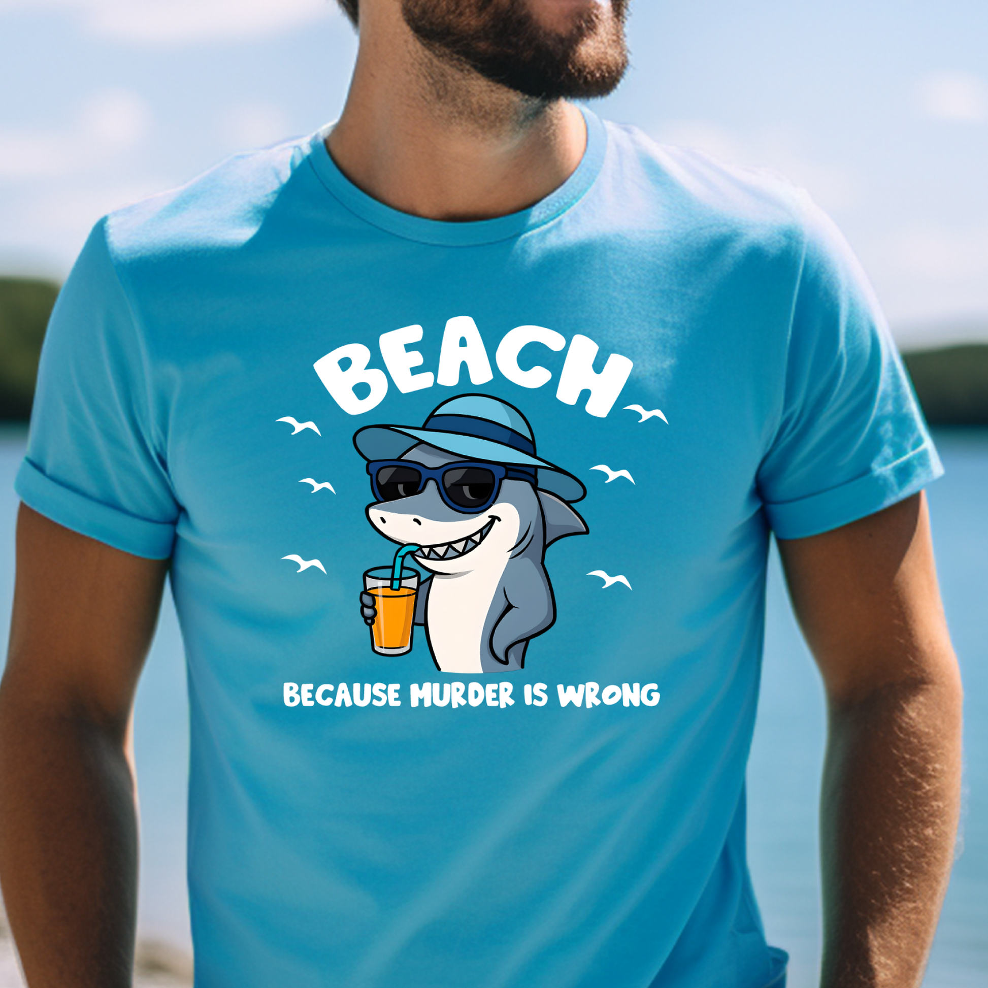 Person wearing a aqua blue t-shirt with a shark graphic and text at a beach.