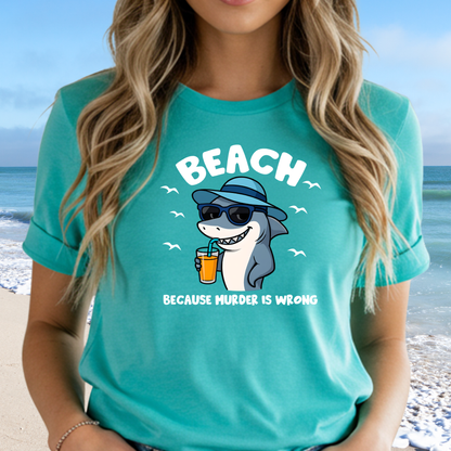 Person wearing a turquoise t-shirt with a shark graphic and text at the beach.