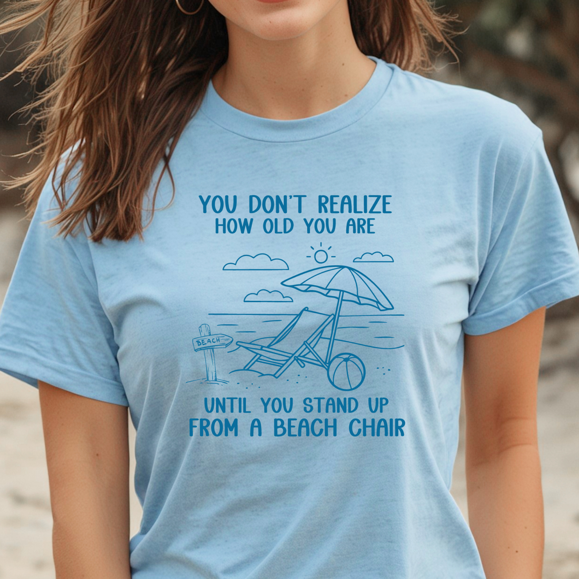 Person wearing a light blue t-shirt with a beach-themed design and text.
