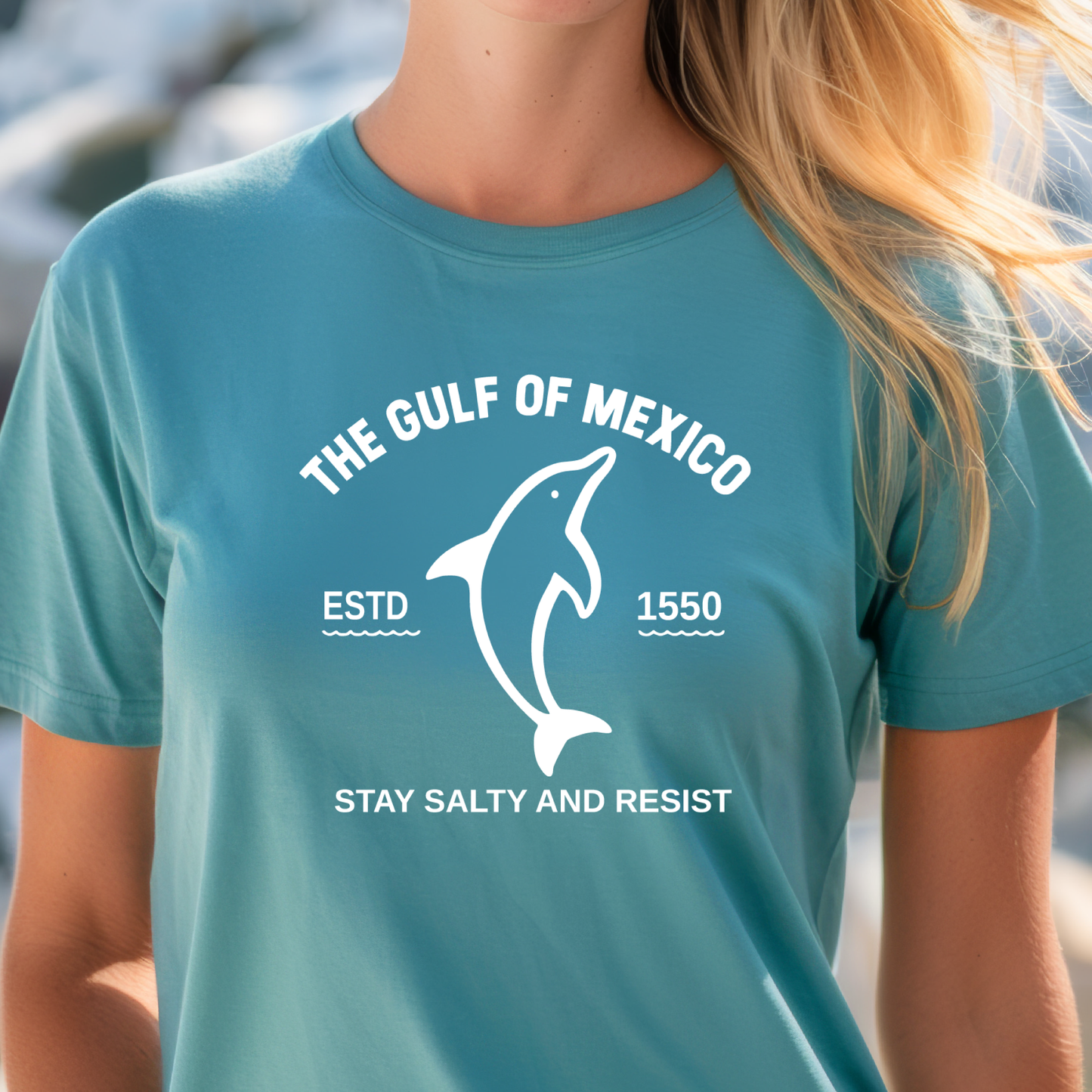 Person wearing a turquoisel t-shirt with a dolphin graphic and text about the Gulf of Mexico.