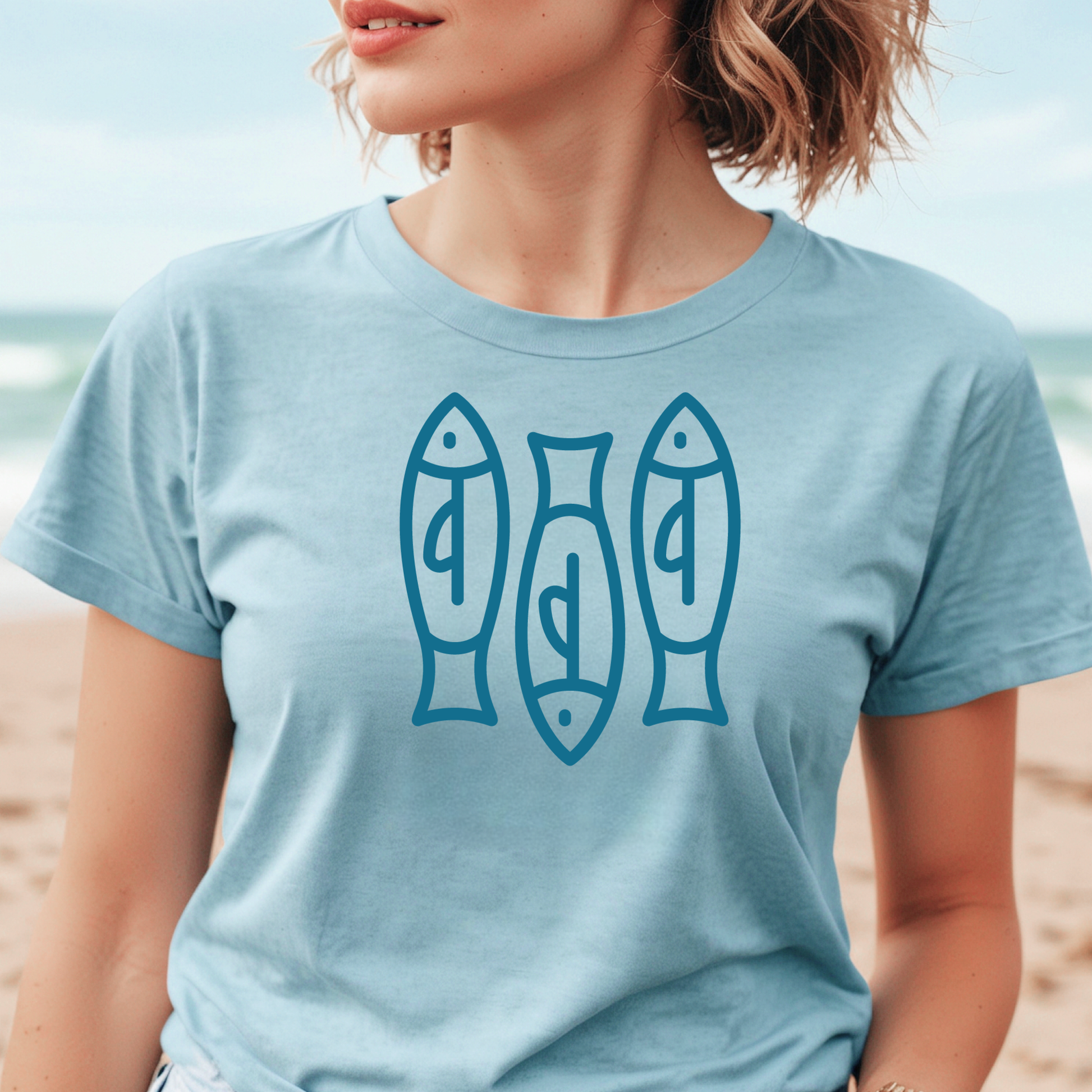 Bella canvas t shirt of a monoline art of  three sardines in one color graphic. Picture of a girl standing on the beach wearing a t shirt.