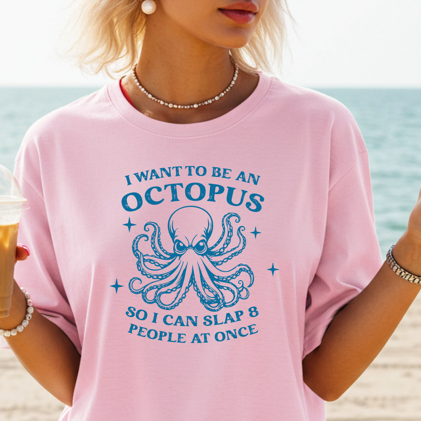 Person wearing a pink t-shirt with an octopus graphic and text on a beach.