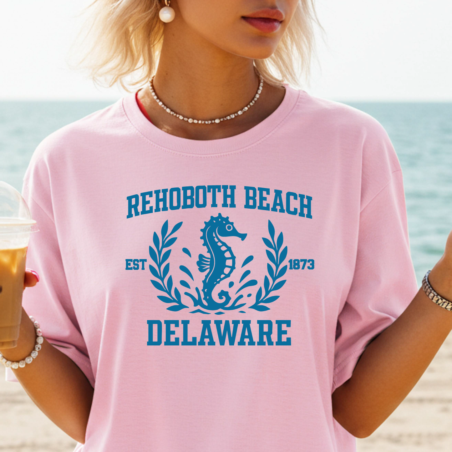 Person wearing a pink t-shirt with Rehoboth Beach, Delaware design on a beach.