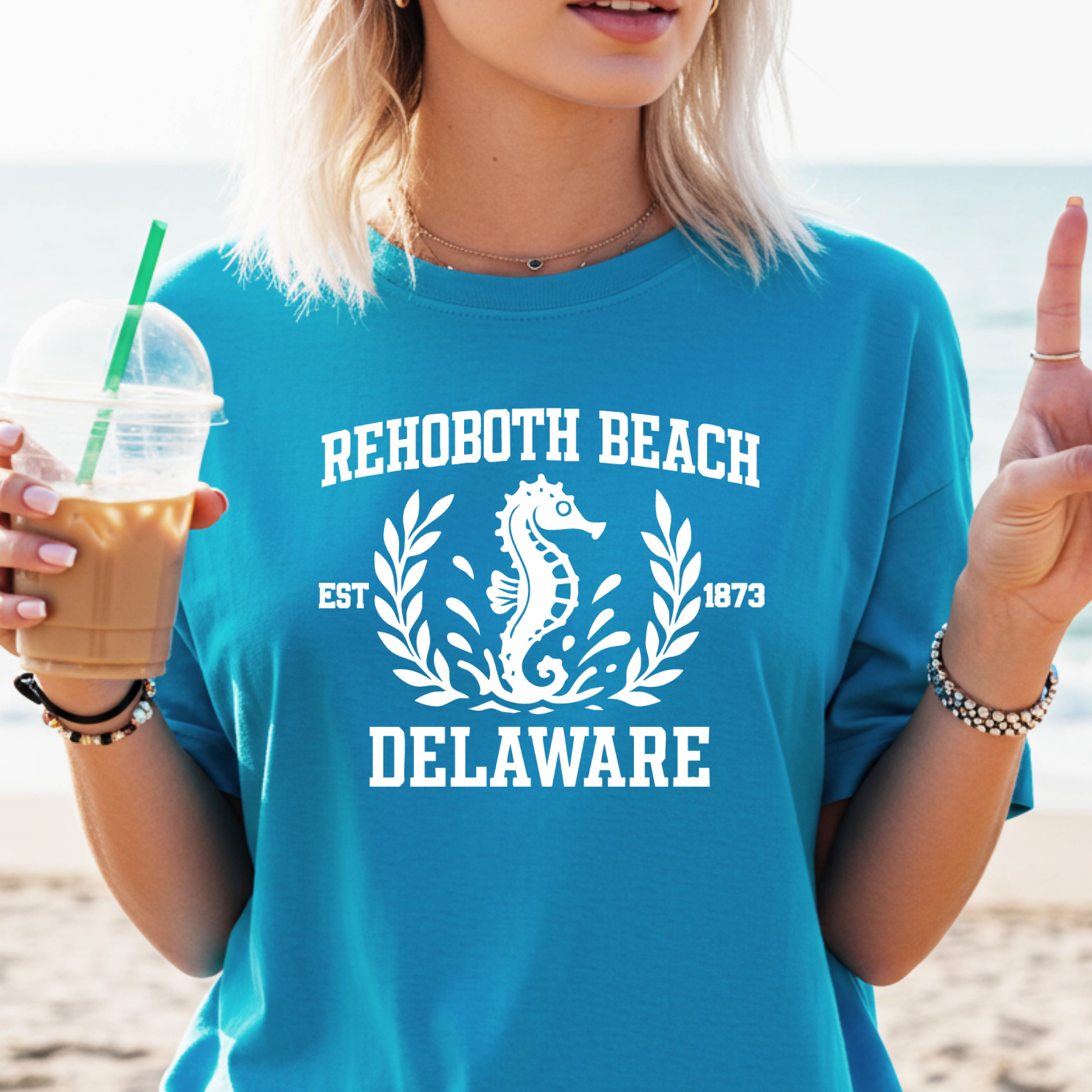Person wearing a blue 'Rehoboth Beach Delaware' t-shirt with a seahorse design on a beach.