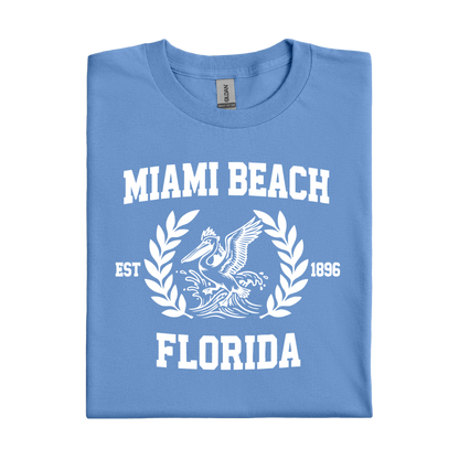 Folded Carolina blue t-shirt with 'Miami Beach Florida' text and pelican design on a white background