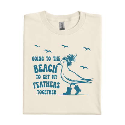 Natural t-shirt with a graphic of a bird and text 'Going to the beach to get my feathers together' on a white background.