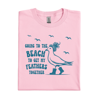 Light Pink t-shirt with a graphic of a bird and text 'Going to the beach to get my feathers together' on a white background.