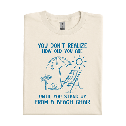 Natural t-shirt with blue beach-themed graphic and text on a white background