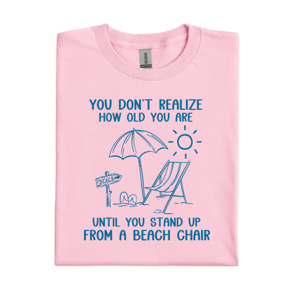 Pink t-shirt with beach-themed design and text on a white background