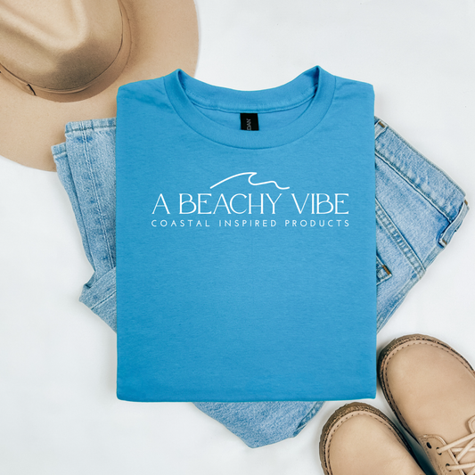 Gildan 5000 "A Beachy Vibe" t shirt with a simple wave graphic in one color. Picture on a flay lay mockup with pair of blue jeans, brown shoes and a hat accessory.