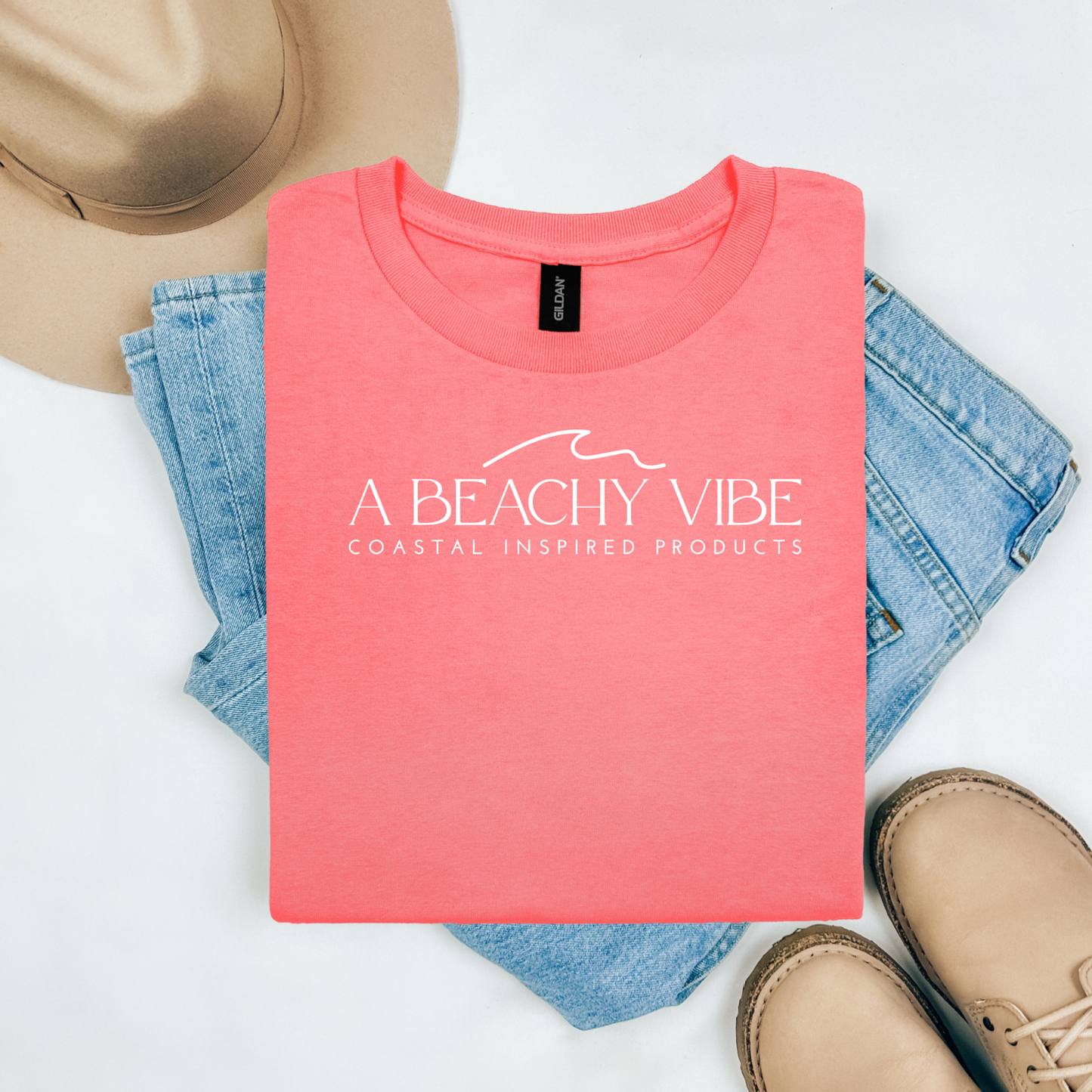 Gildan 5000 "A Beachy Vibe" t shirt with a simple wave graphic in one color. Picture on a flay lay mockup with pair of blue jeans, brown shoes and a hat accessory.