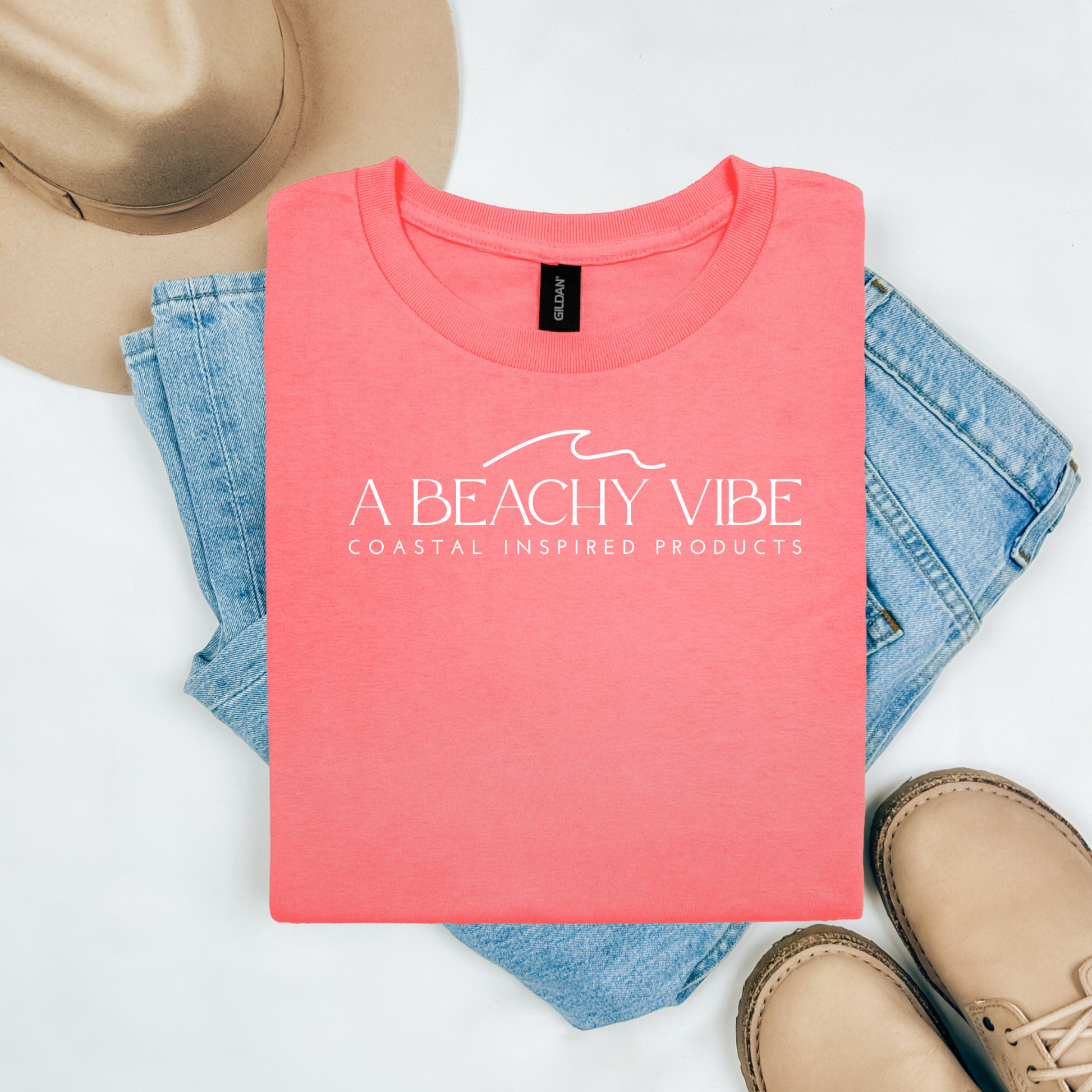 Gildan 5000 "A Beachy Vibe" t shirt with a simple wave graphic in one color. Picture on a flay lay mockup with pair of blue jeans, brown shoes and a hat accessory.