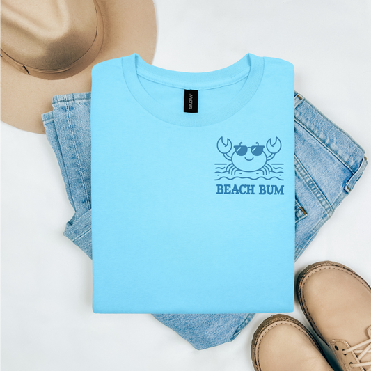 Gildan 5000 "Beach Bum" t shirt with a crab on the beach graphics in one color. Picture on a flay lay mockup with pair of blue jeans, brown shoes and a hat accessory.