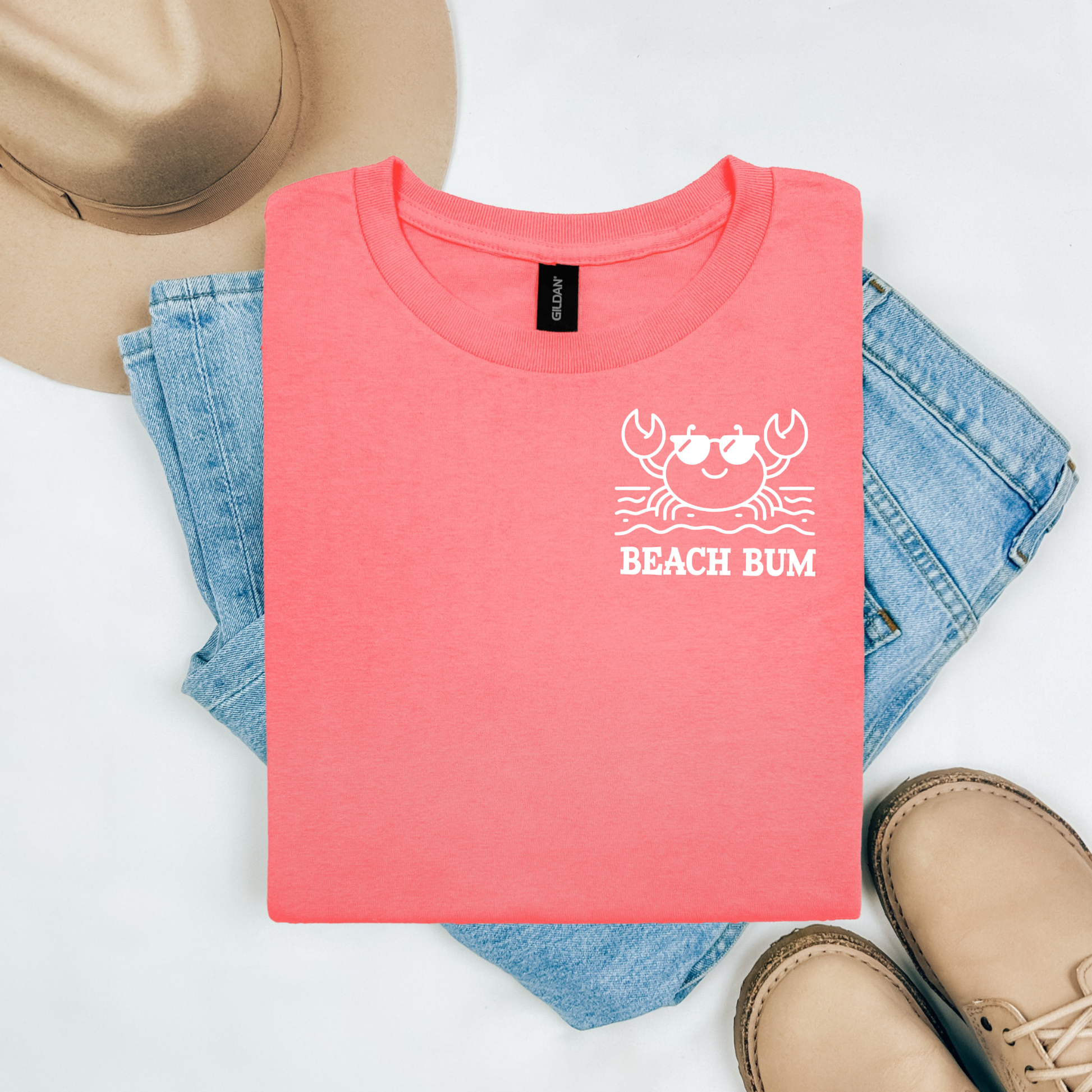 Gildan 5000 "Beach Bum" t shirt with a crab on the beach graphics in one color. Picture on a flay lay mockup with pair of blue jeans, brown shoes and a hat accessory.