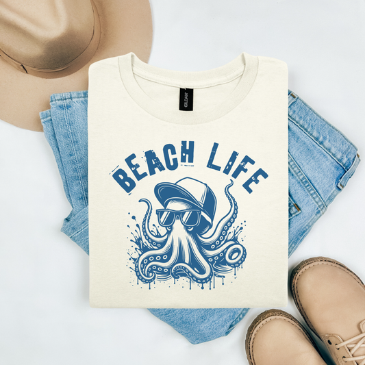Gildan 5000 "Beach Life" t shirt with cute octopus wearing a baseball cap and  sunglasses in one color. Picture on a flay lay mockup with pair of blue jeans, brown shoes and a hat accessory.