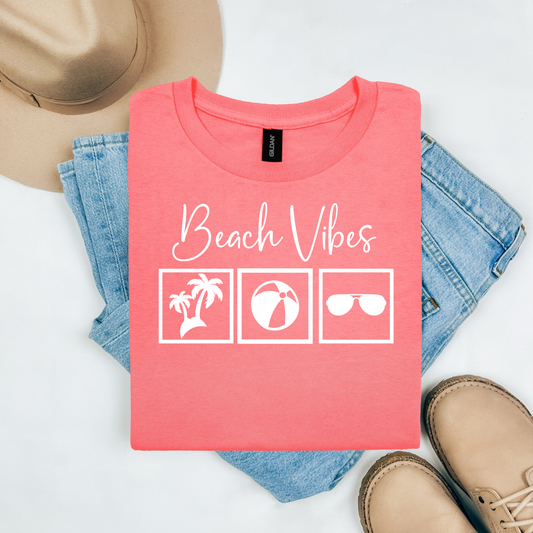 Gildan 5000 "Beach Vibes" t shirt with a palm tree, beach ball, and sunglasses graphics in monochrome color. Picture on a flay lay mockup with pair of blue jeans, brown shoes and a hat accessory.
