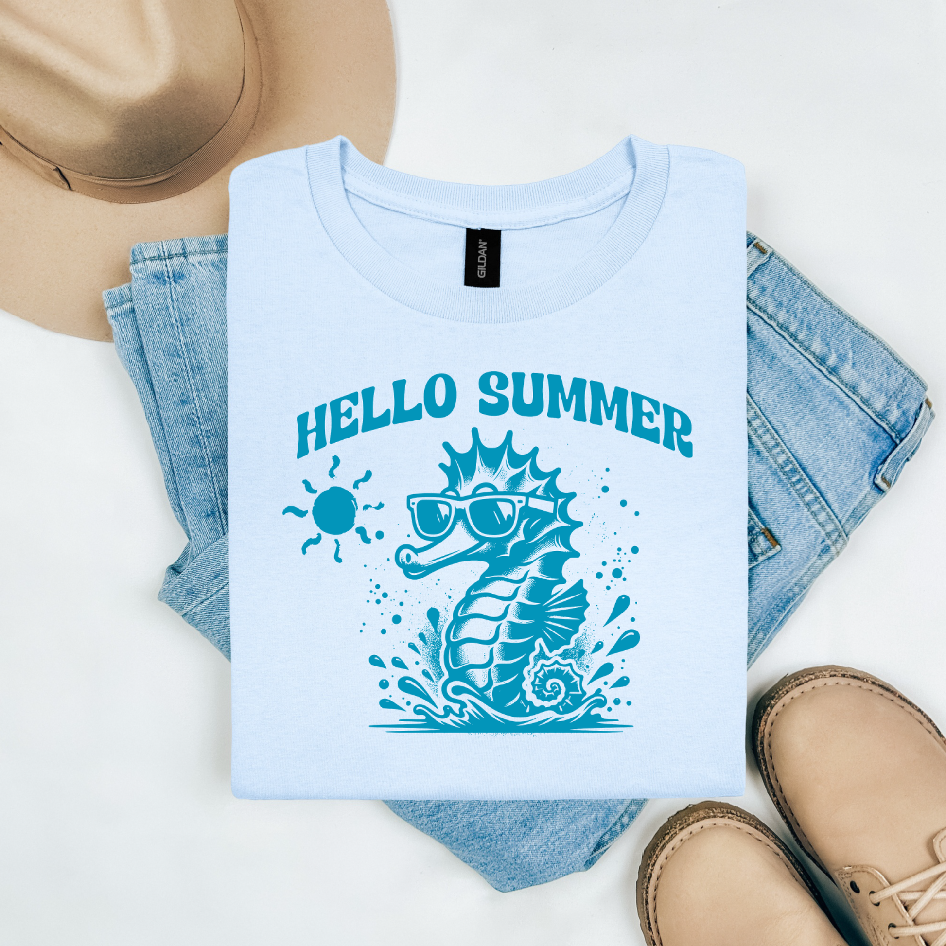 Gildan 5000 "Hello Summer" t shirt with a cute seahorse with sunglasses in one color graphics. Picture on a flay lay mockup with pair of blue jeans, brown shoes and a hat accessory.