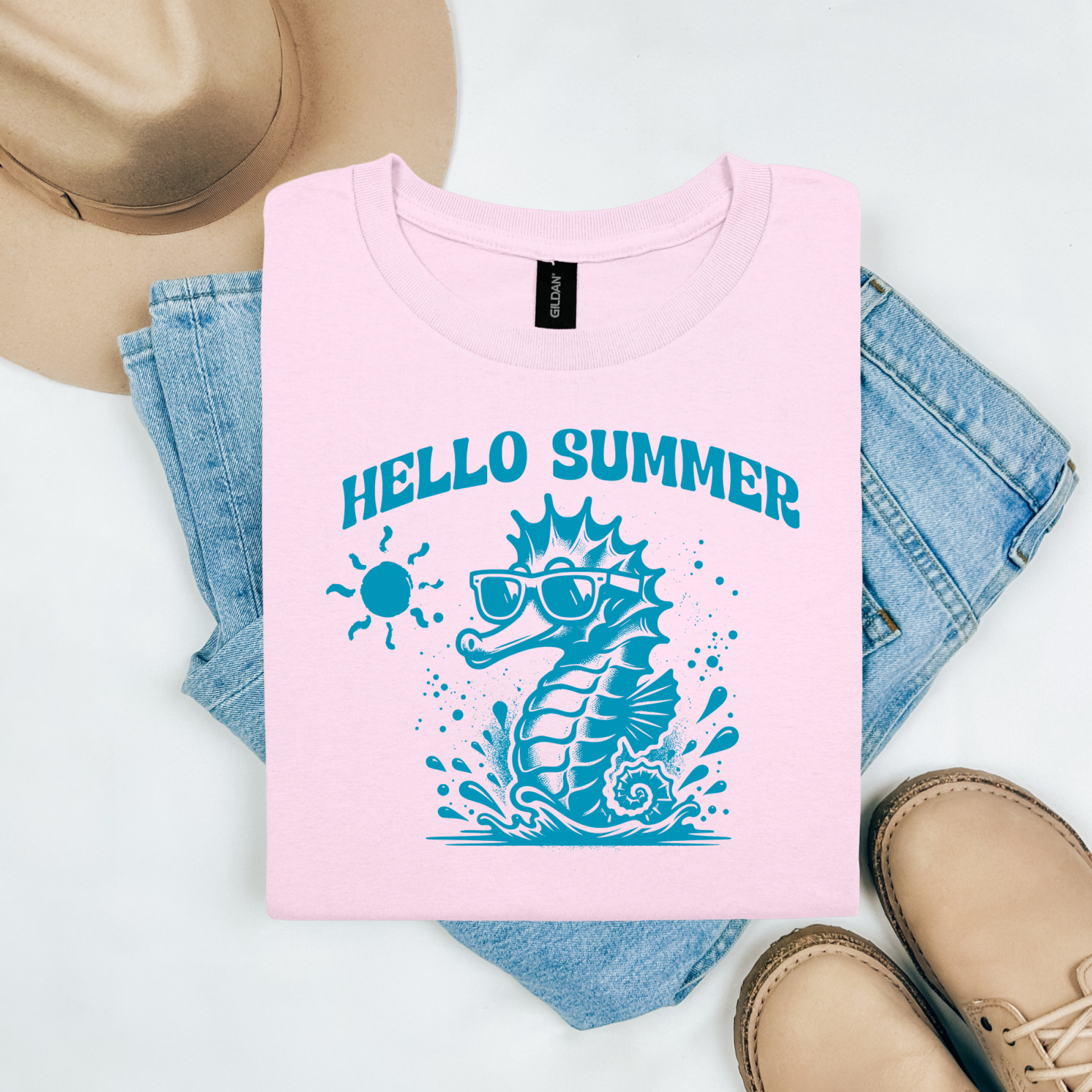 Gildan 5000 "Hello Summer" t shirt with a cute seahorse with sunglasses in one color graphics. Picture on a flay lay mockup with pair of blue jeans, brown shoes and a hat accessory.