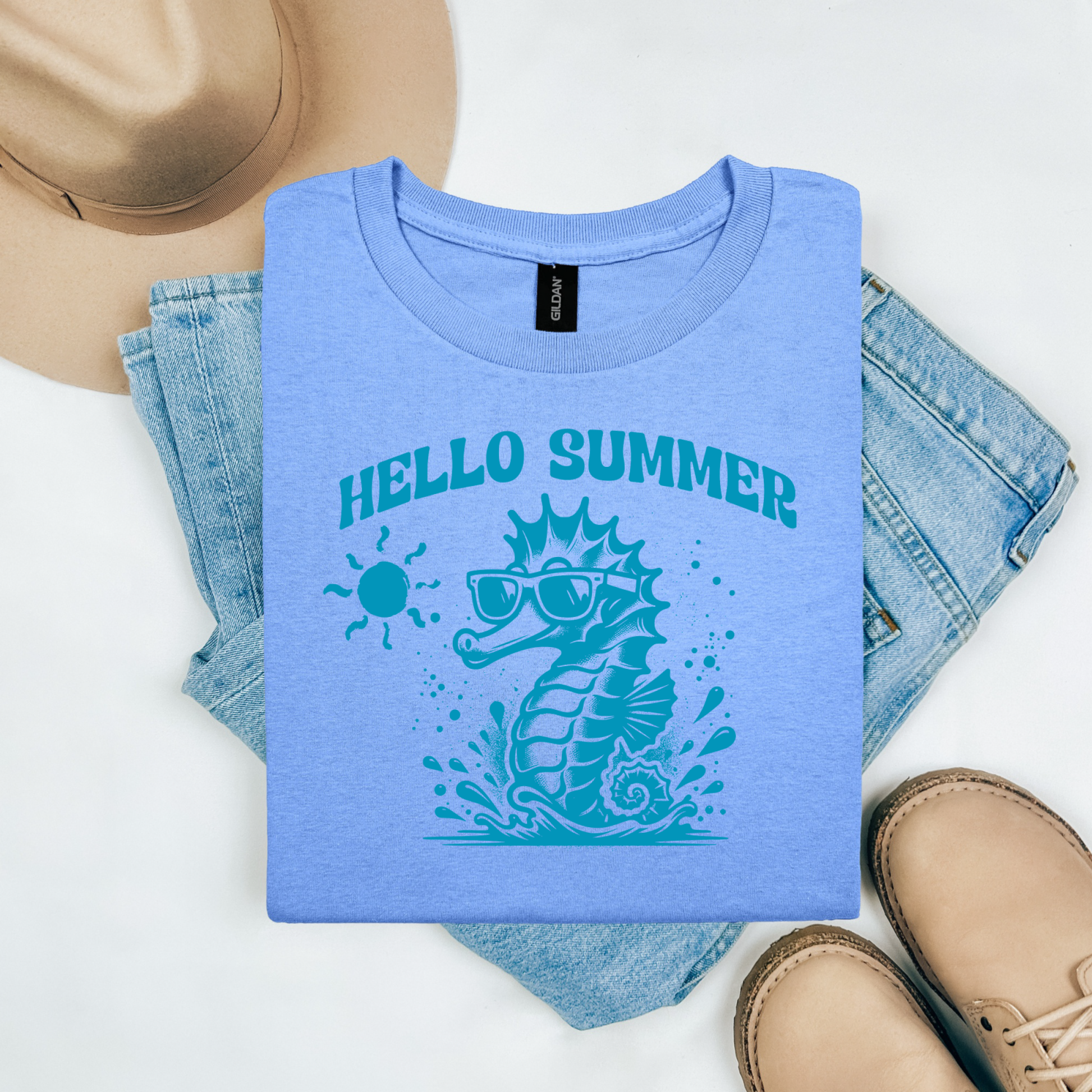 Gildan 5000 "Hello Summer" t shirt with a cute seahorse with sunglasses in one color graphics. Picture on a flay lay mockup with pair of blue jeans, brown shoes and a hat accessory.