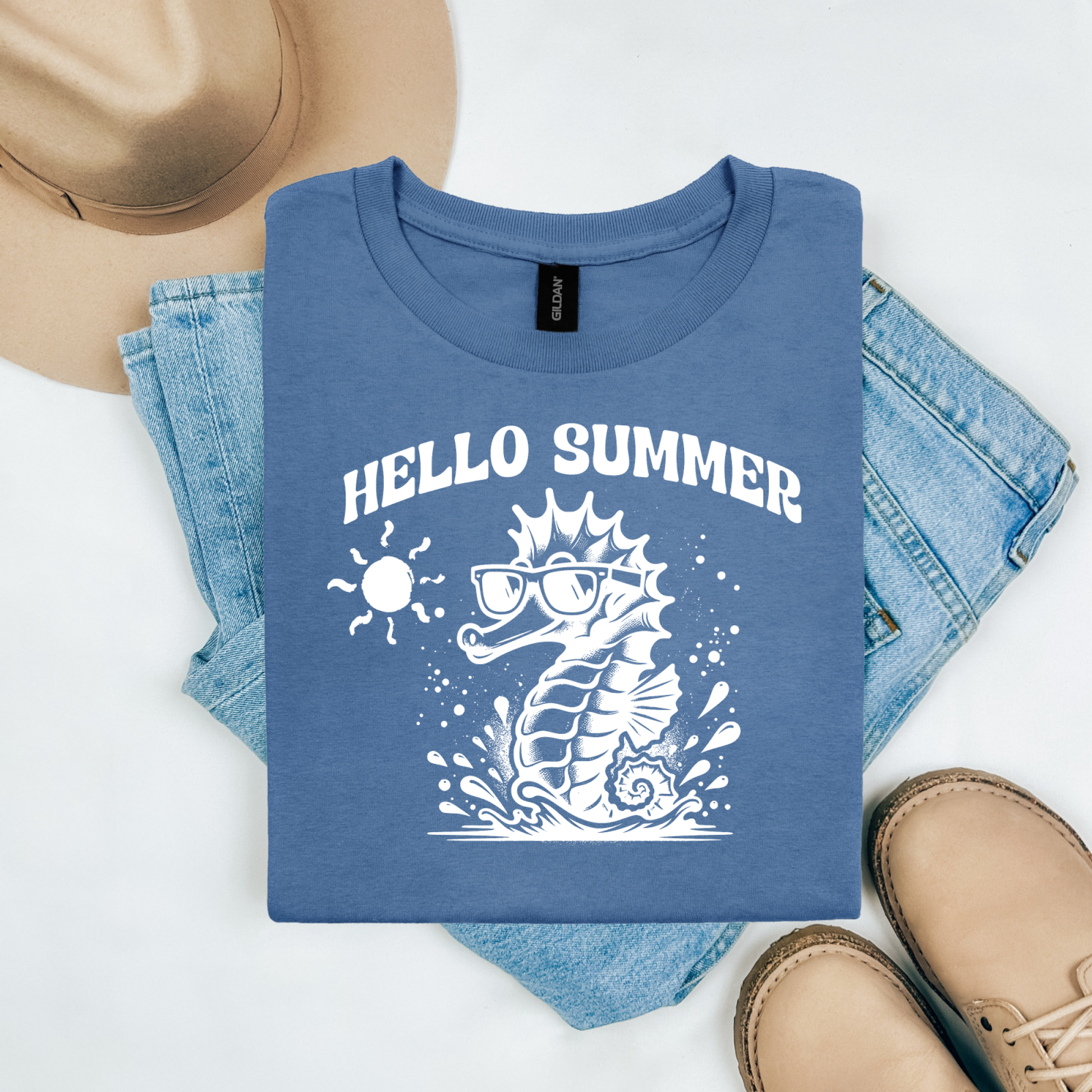 Gildan 5000 "Hello Summer" t shirt with a cute seahorse with sunglasses in one color graphics. Picture on a flay lay mockup with pair of blue jeans, brown shoes and a hat accessory.