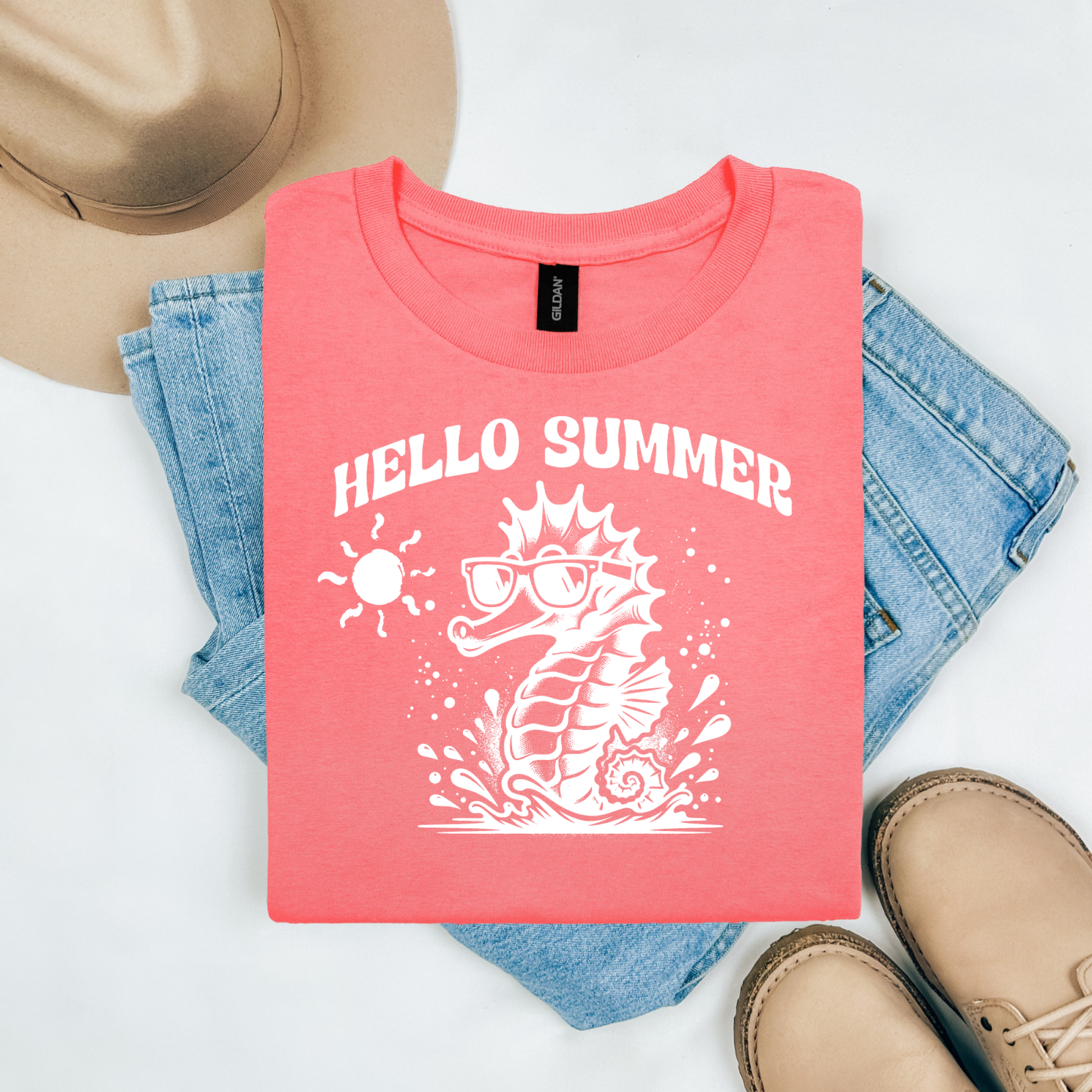 Gildan 5000 "Hello Summer" t shirt with a cute seahorse with sunglasses in one color graphics. Picture on a flay lay mockup with pair of blue jeans, brown shoes and a hat accessory.