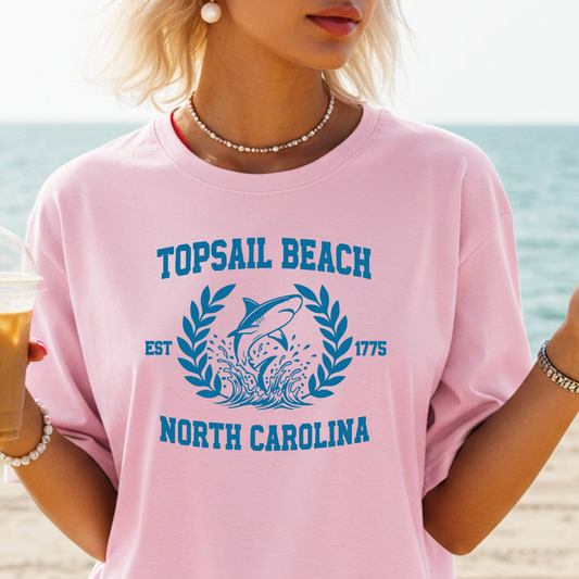 Person wearing a pink 'Topsail Beach, North Carolina' t-shirt with a beach background