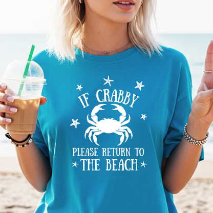 Person wearing a sapphire blue t-shirt with a crab graphic and text on a beach.