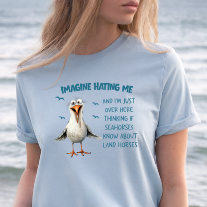 Person wearing a light blue t-shirt with a cartoon seagull and humorous text by a body of water.