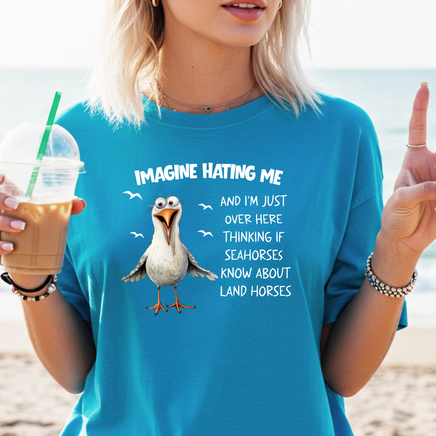 Person wearing a sapphire blue t-shirt with a cartoon seagull and humorous text on a beach.