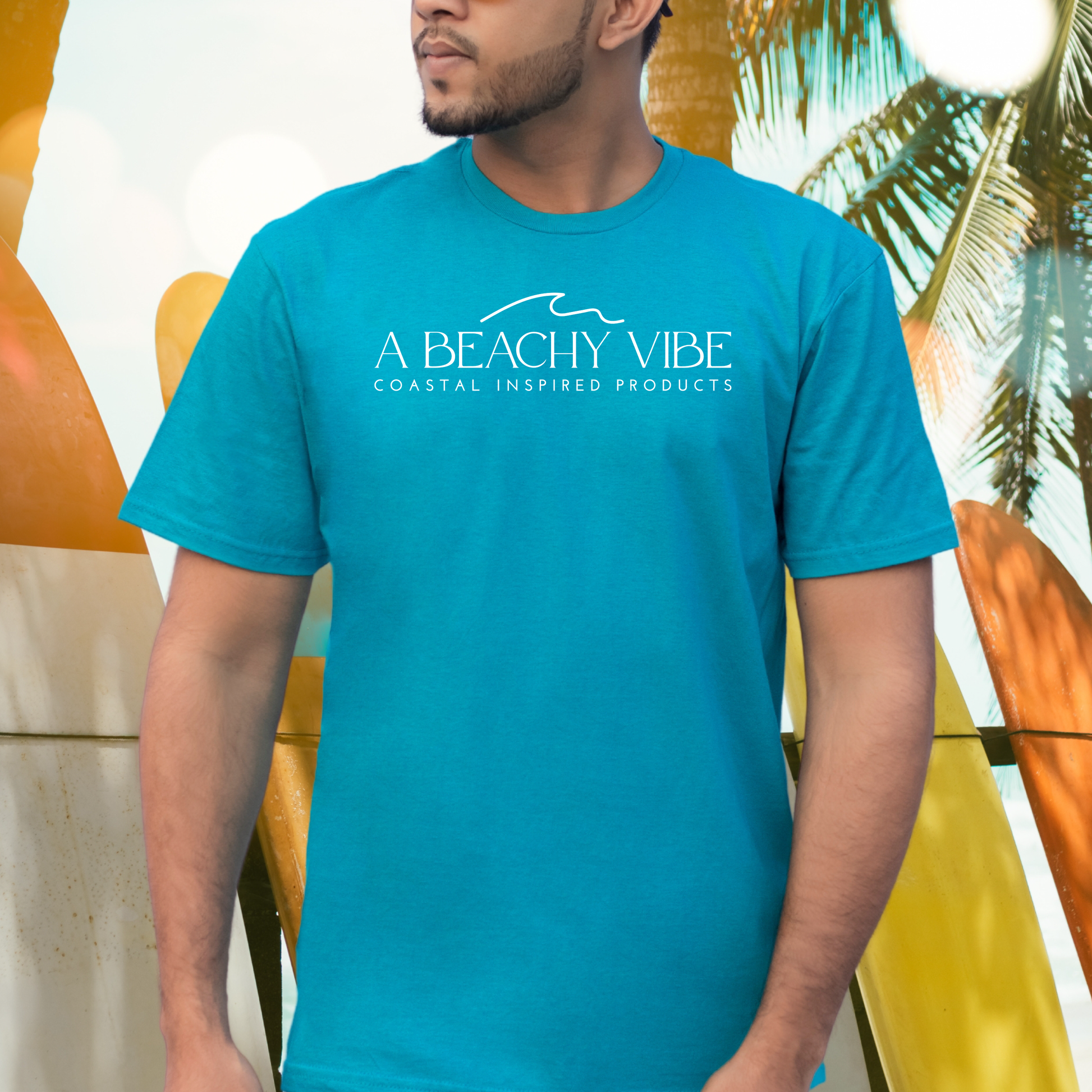 Gildan 5000 "A Beachy Vibe" t shirt with a simple wave graphic in one color. Picture of a man standing next to surfboards wearing a t shirt.
