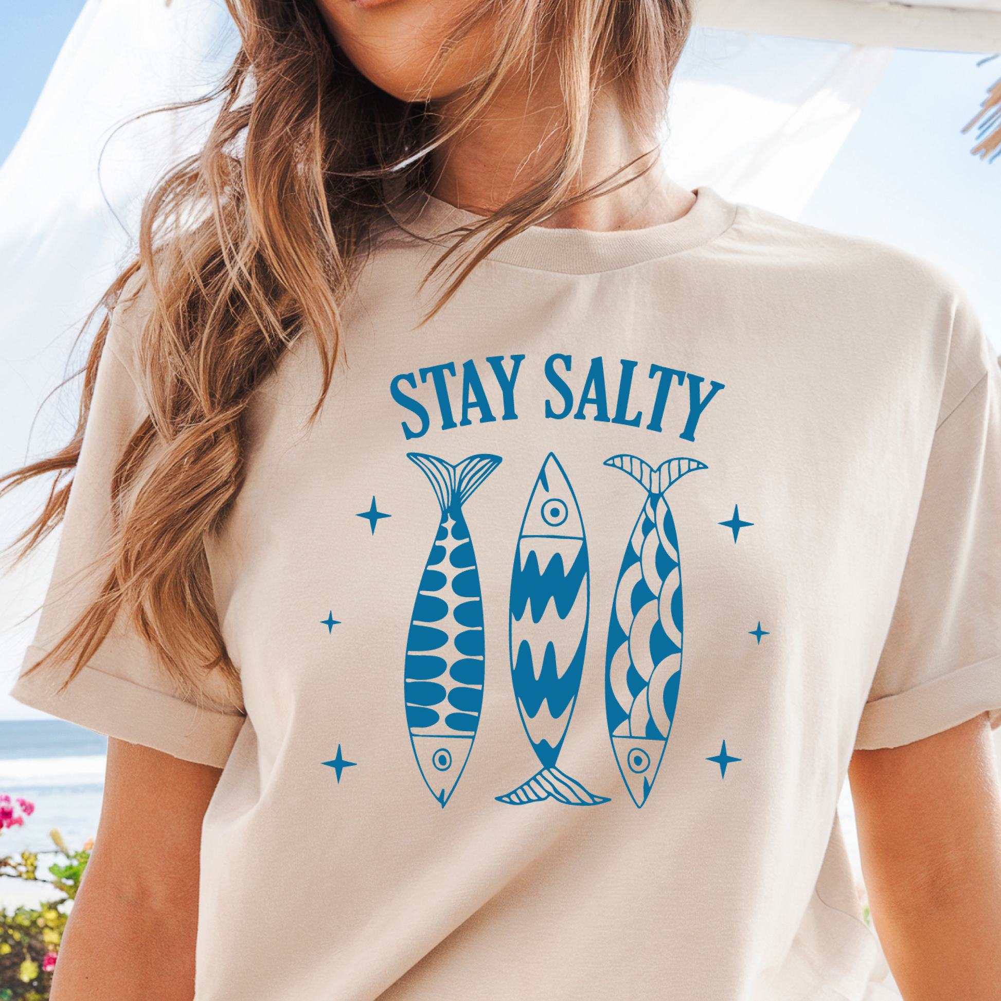 Person wearing a natural t-shirt with 'Stay Salty' and fish graphics.