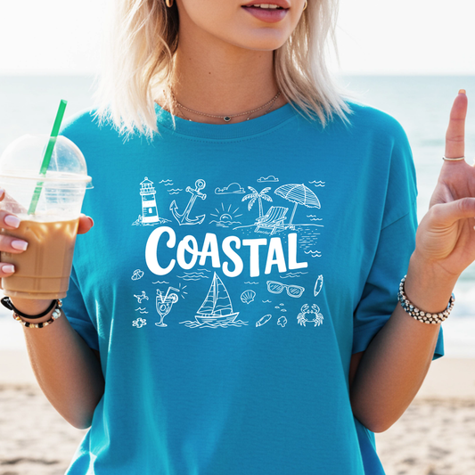 Person wearing a blue t-shirt with 'Coastal' design on a beach