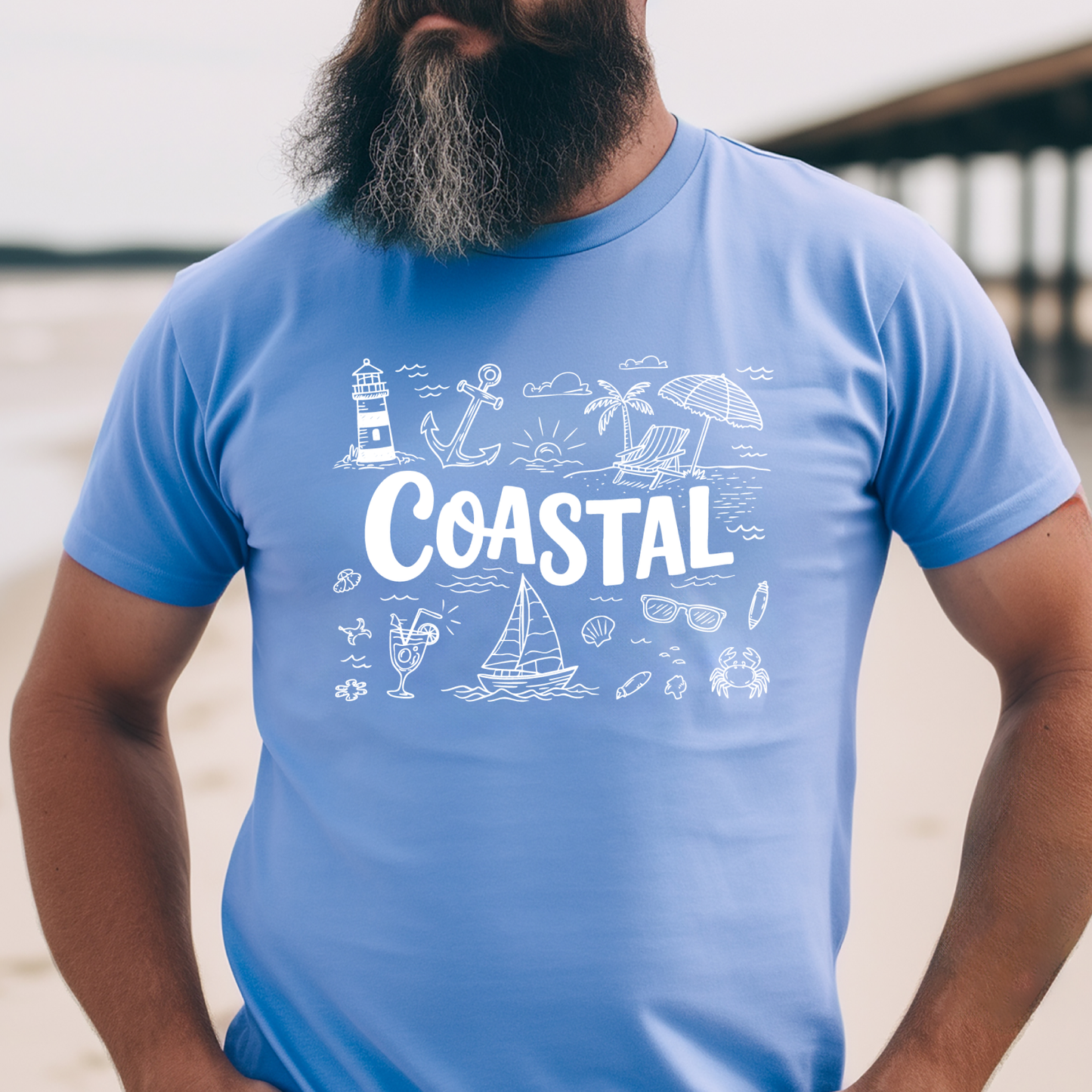 Person wearing a Carolina blue t-shirt with 'Coastal' design featuring beach elements.