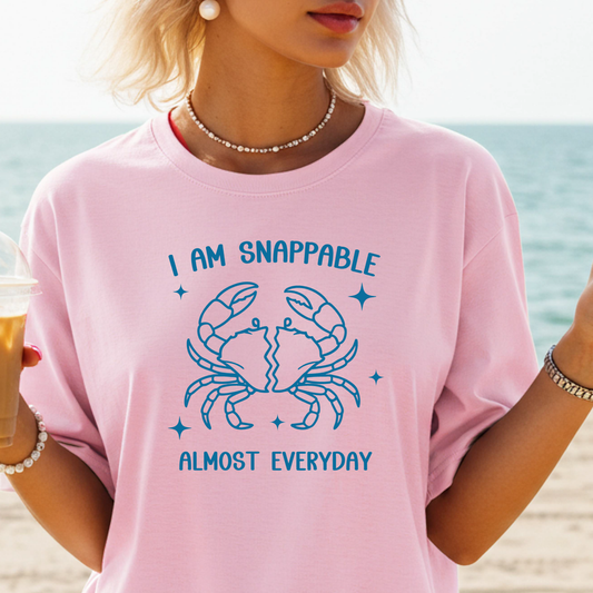 Person wearing a pink t-shirt with a blue crab graphic and text on a beach.