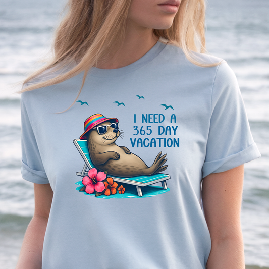 Person wearing a light blue t-shirt with a seal graphic and text by a body of water.